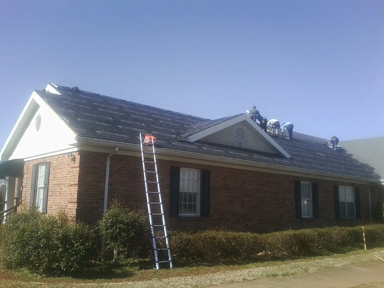 Crew tearing shingles off a brick ranch roof with a ladder set — Metal Roof Repair work by our crew in Wellsville