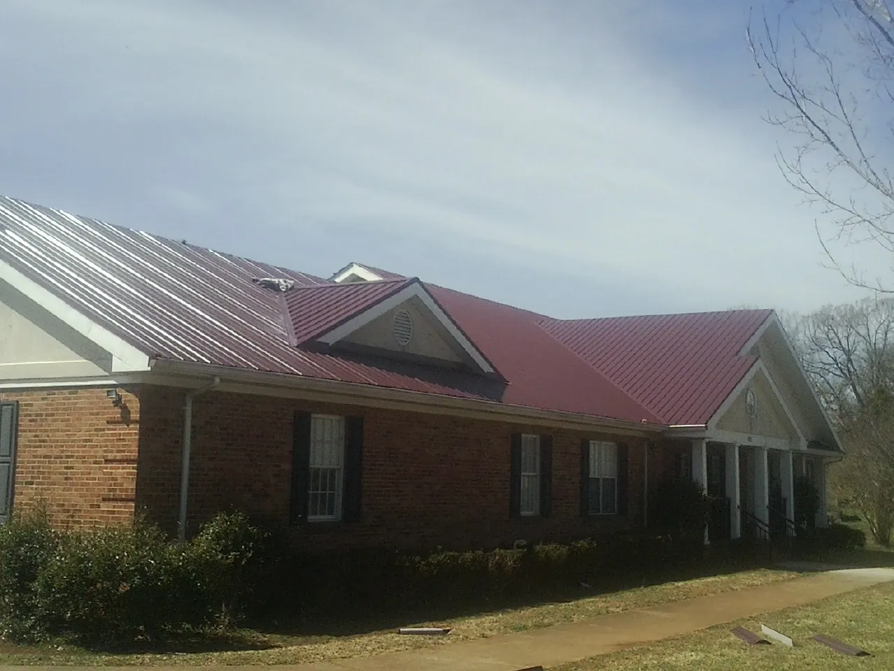 Red metal roof with gabled entries on a long brick building, from a Hail Damage Roof Repair job in Wellsville