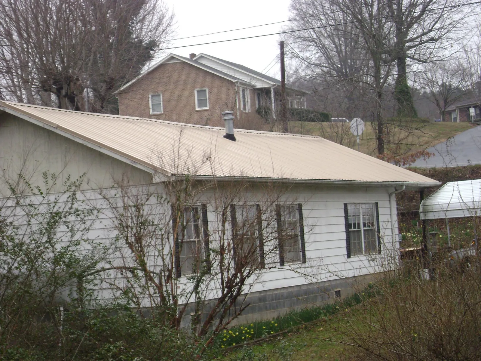Tan metal roof on a white sided house set into a hillside — Commercial Roofing by Roofing Brothers in Wellsville